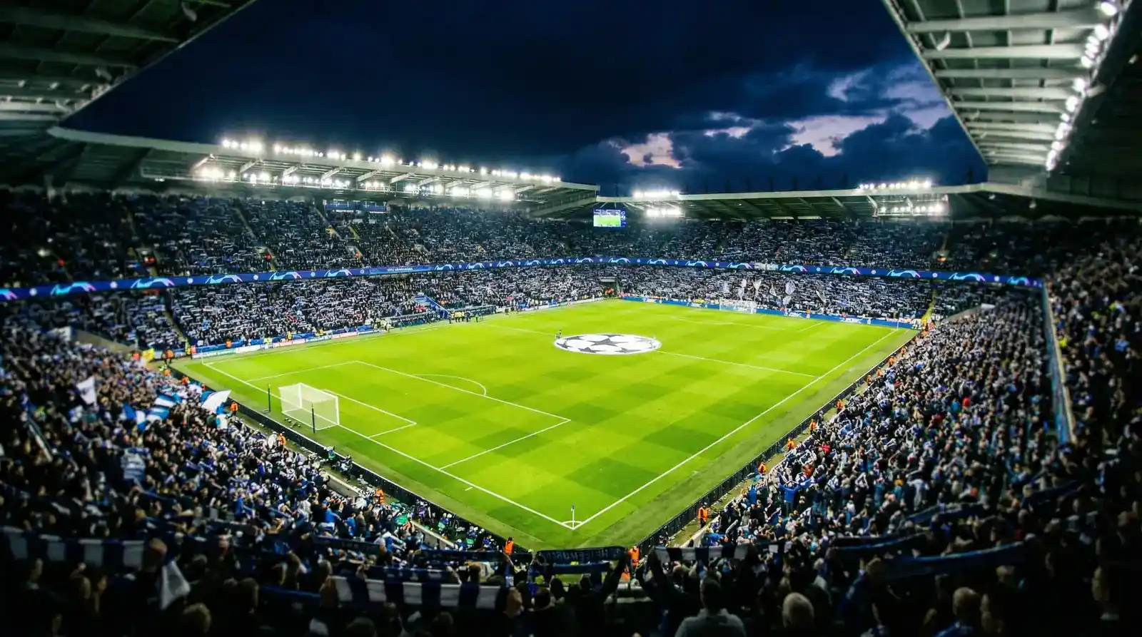 Estádio de futebol iluminado durante jogo da Champions League com atmosfera nocturna
